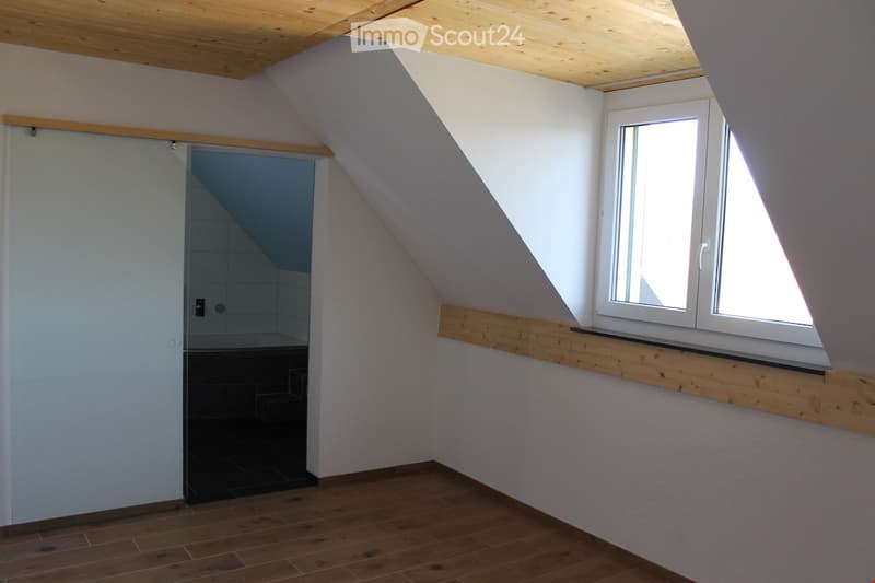 Unfurnished Room. An empty attic room with wooden flooring, white walls, a wooden ceiling, a sliding door, and a window with a wooden sill.