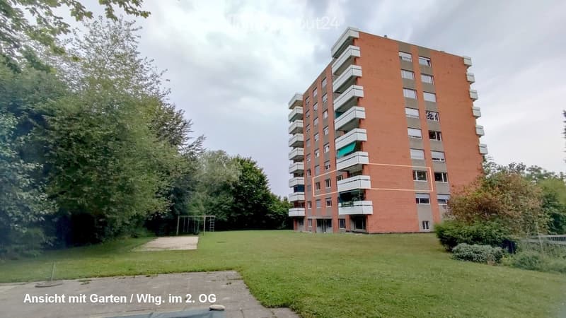 A multi-story building with brick facade, balconies, and a green lawn in front.