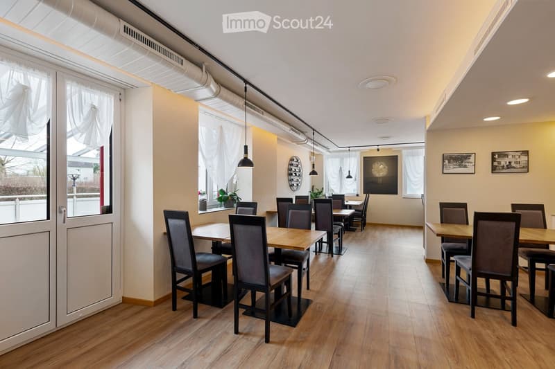Dining room with wooden floor, wooden tables, chairs, white curtains, white walls, ceiling lamps, plants, framed pictures