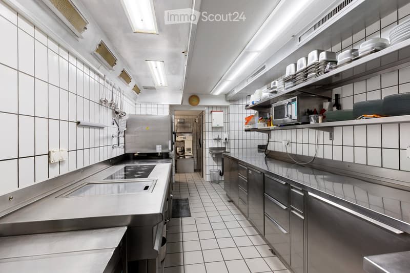 Stainless steel countertops, white tiled walls, stainless steel appliances, two ovens, a microwave, various utensils, a sink, storage shelves