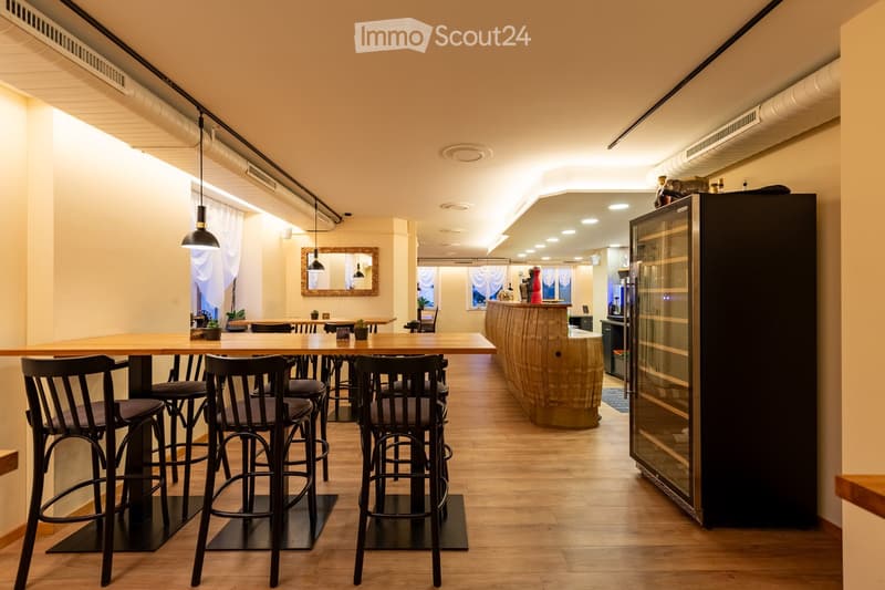 wooden floor, wooden bar counter, black chairs and bar stools, large mirror, wooden tables, black cabinet