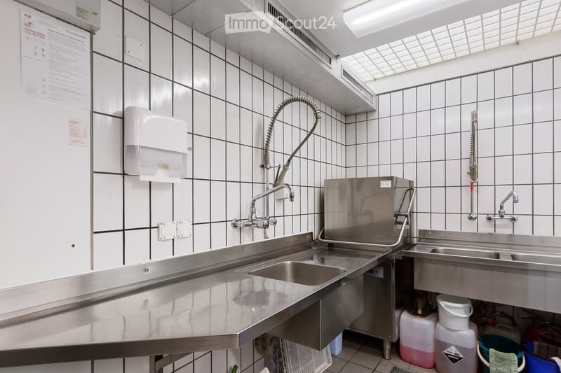 commercial kitchen with stainless steel countertops, two sinks, faucets, a hand dryer, and cleaning supplies