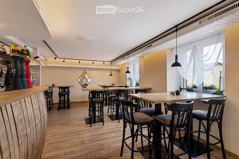 wooden floor, white walls, black chairs and stools, round wooden tables, large windows, hanging lamps, decorative items