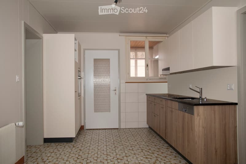 Modern kitchen with white cabinets, wooden countertops, tiled floor, and a white door leading to another room.
