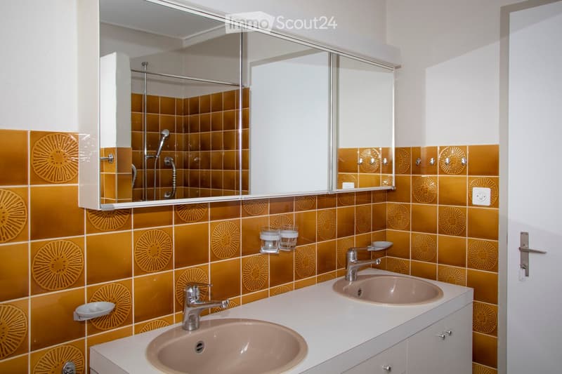 Bathroom with double sinks, mirror, and tiled walls.