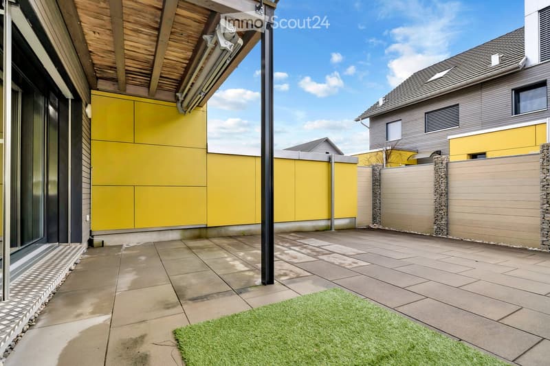 Outdoor area with a tiled floor, yellow walls, and a green artificial grass patch. A black pole stands in the center.