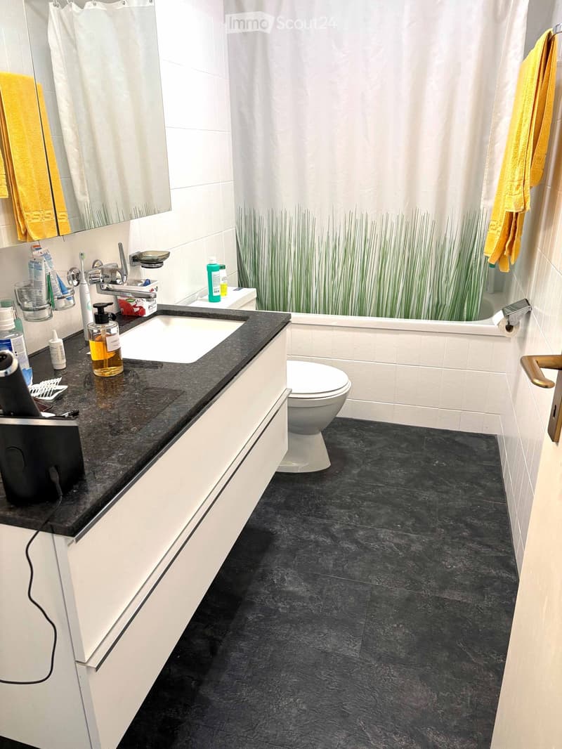 Bathroom with white tiles, black countertop, white sink, white toilet, and a shower curtain with a grass design.