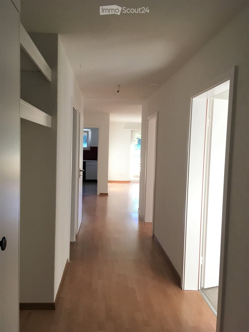 Empty corridor with white walls, wooden floor, and doors on both sides.
