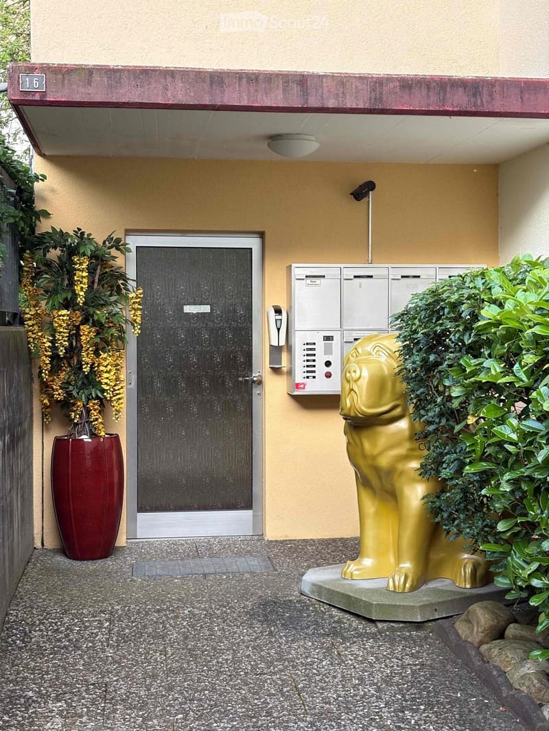 Entrance area of a building with a modern door, mailboxes, a golden lion statue, and potted plants.