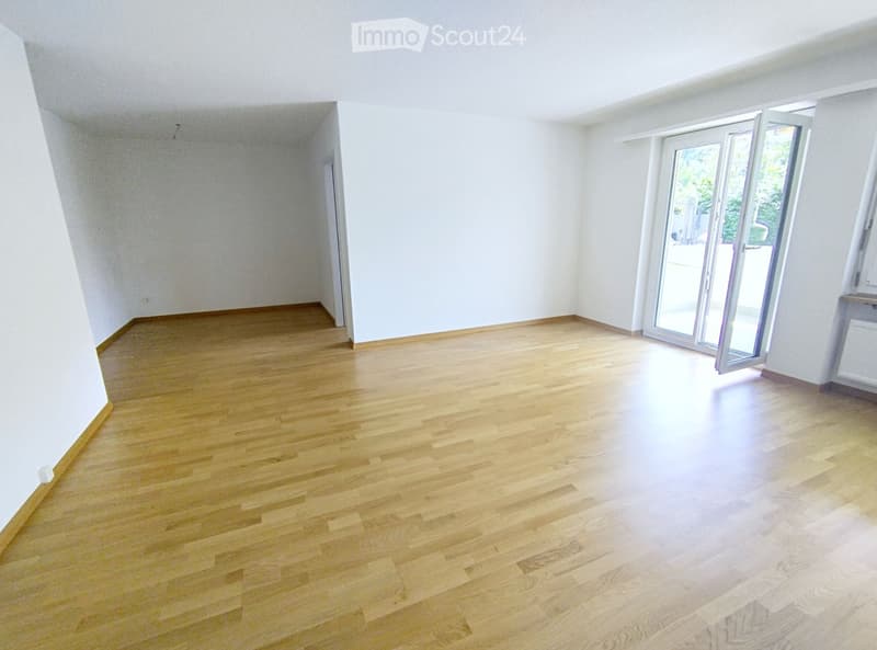 Empty room with light wooden flooring and white walls, featuring large glass sliding doors leading outside.