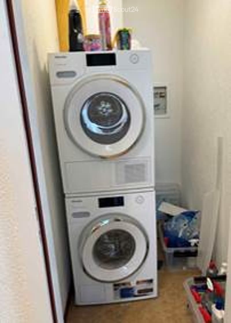 A small room with stacked washing machine and dryer, storage boxes, and various items on the floor.