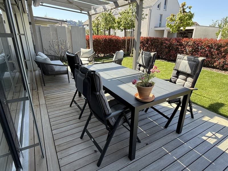 Garden / Outdoor Area. A wooden deck with a table and chairs, a potted plant with flowers, and a grassy area with bushes.