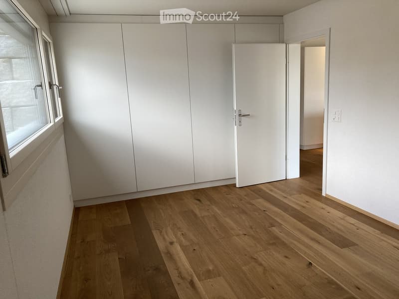 Unfurnished Room. An empty room with white walls, wooden floor, and a white door. There are built-in white cabinets on the left side, and a window on the left wall.