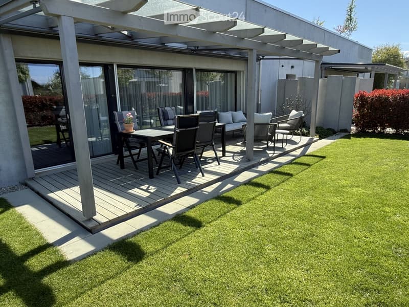 Garden / Outdoor Area. Outdoor patio with wooden deck, table, chairs, and sofa with cushions. Green lawn and pergola.