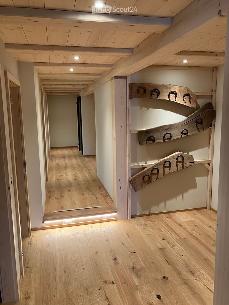 Wooden hallway with exposed beams, light-colored wooden flooring, built-in wooden storage unit with hooks, and recessed lighting.