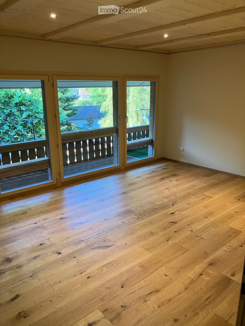 Empty room with light wooden flooring and large sliding glass doors leading to a balcony.