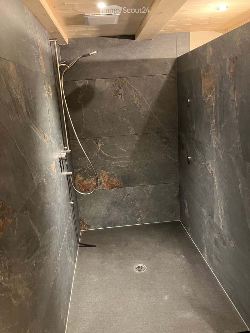 Modern shower area with dark grey marble tiles on walls and floor, featuring a handheld showerhead and a built-in drain.