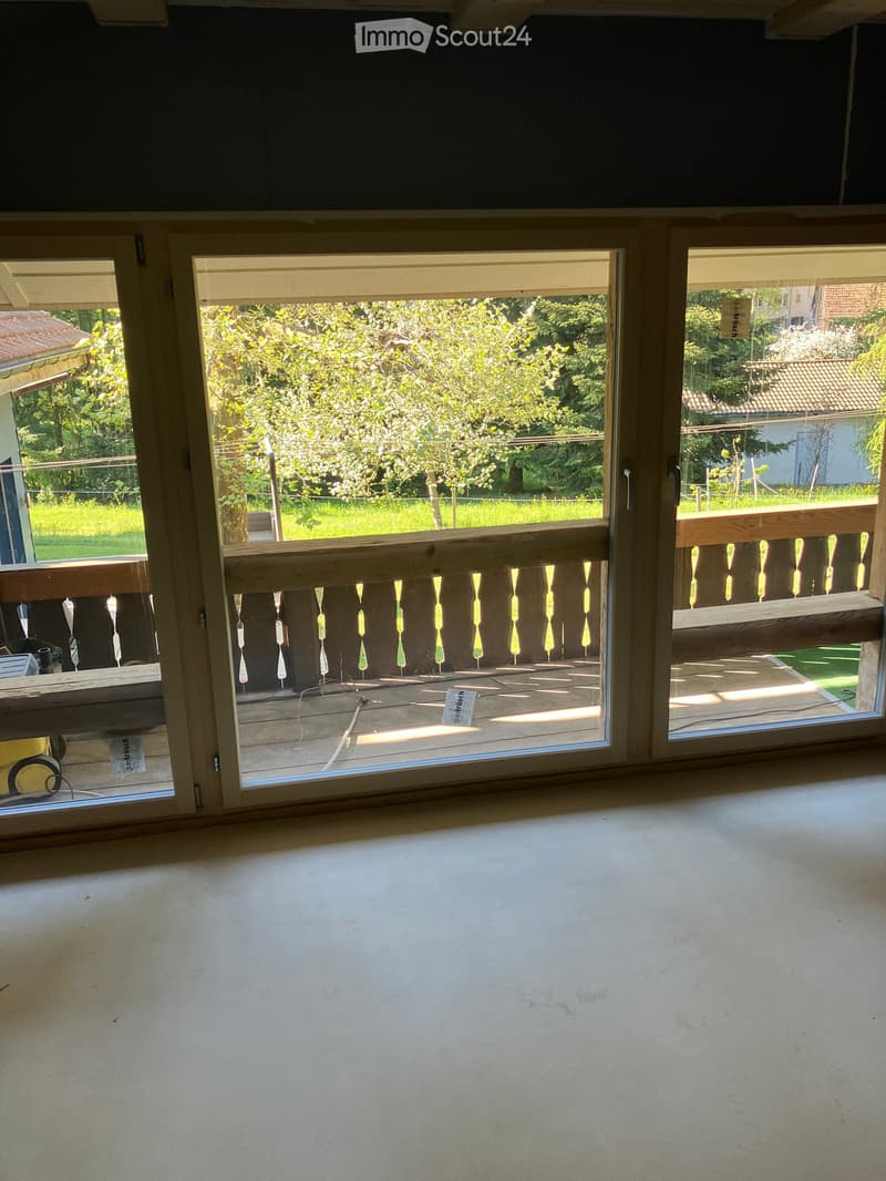 Unfurnished Room. An empty room with large windows and a balcony. The room has a white floor and a wooden balcony with a railing. Outside, there is a grassy area with trees and a house in the distance.