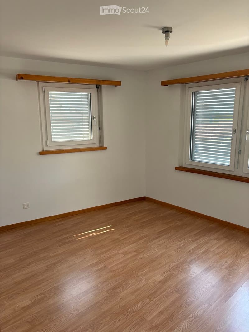 Empty room with wooden flooring, white walls, and two windows with blinds. Wooden shelves above the windows.