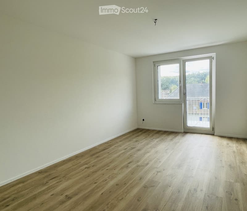 Empty room with white walls, wooden floor, and a sliding glass door leading to a balcony.