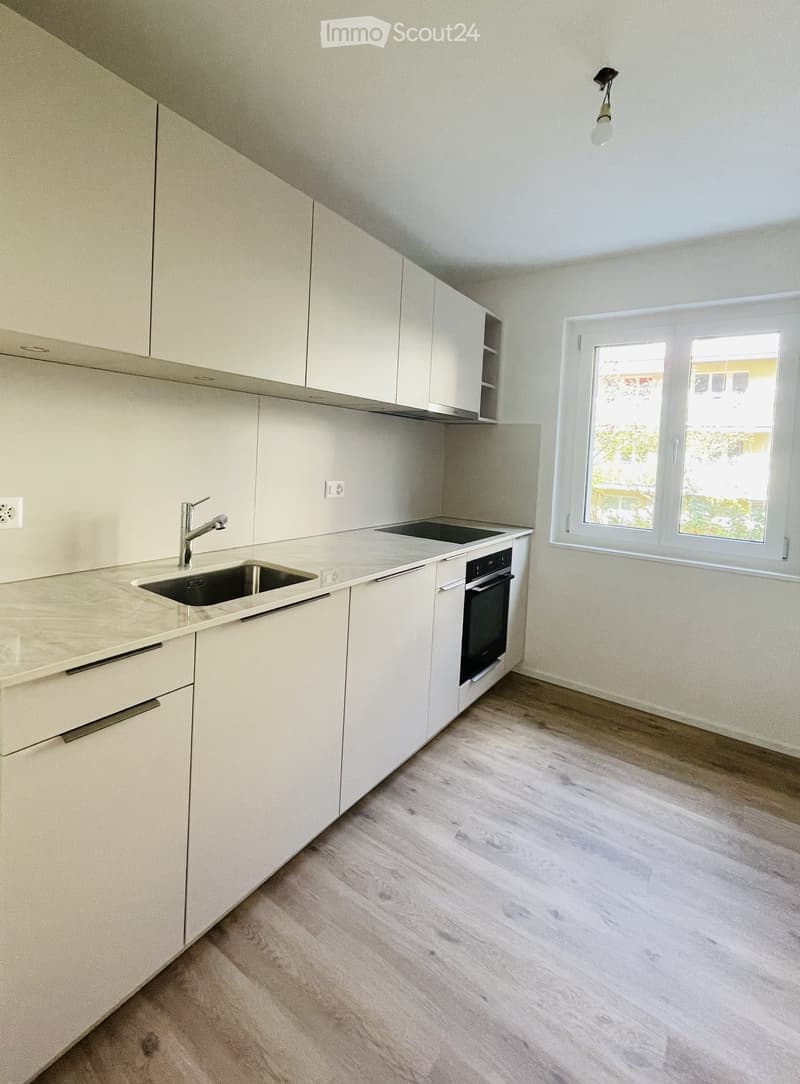 Modern kitchen with white cabinets, marble countertop, stainless steel sink, and black stove.