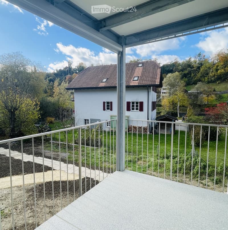 A balcony with a metal railing and a view of a house and a grassy area.
