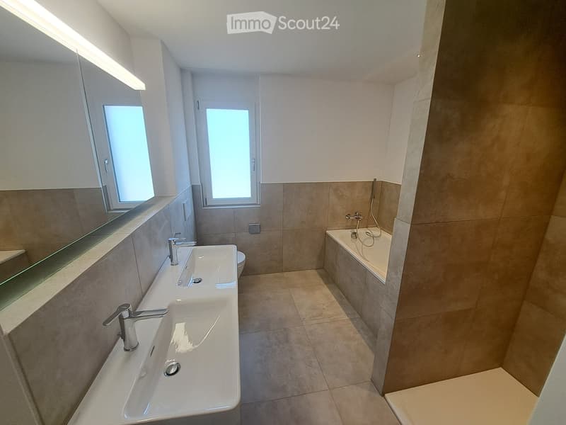 Modern bathroom with double sink, mirror, toilet, bathtub, and shower area.