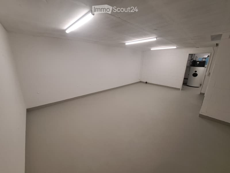 Empty room with white walls, gray floor, and three ceiling lights.