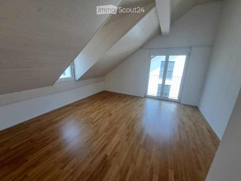 Empty room with wooden floors, white walls, and a glass door leading to a balcony. There are two windows, one of which is on the sloped ceiling.