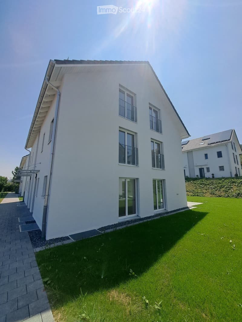 Modern white house with multiple windows and balconies, solar panels on the roof, surrounded by a well-maintained lawn.