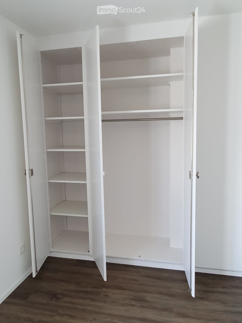 An empty white wardrobe with multiple shelves and a hanging rod, placed against a white wall and wooden floor.