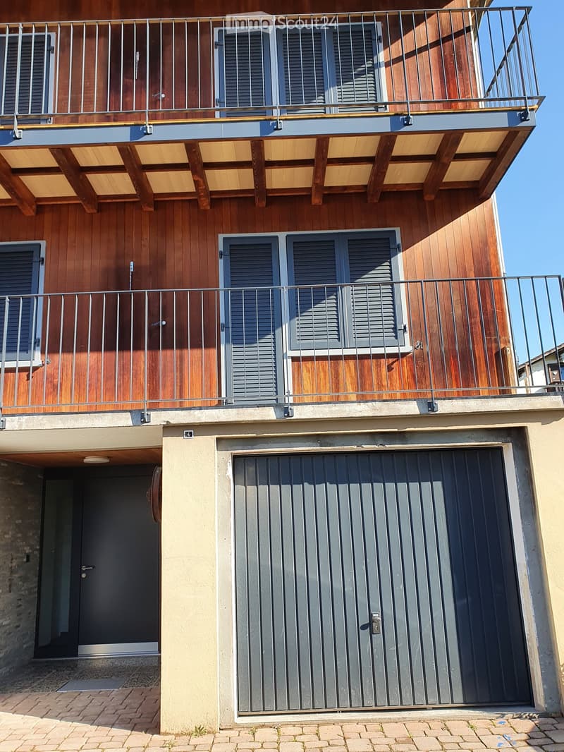 Facade of a two-story building with wooden exterior, metal railings on the balconies, and a garage door.