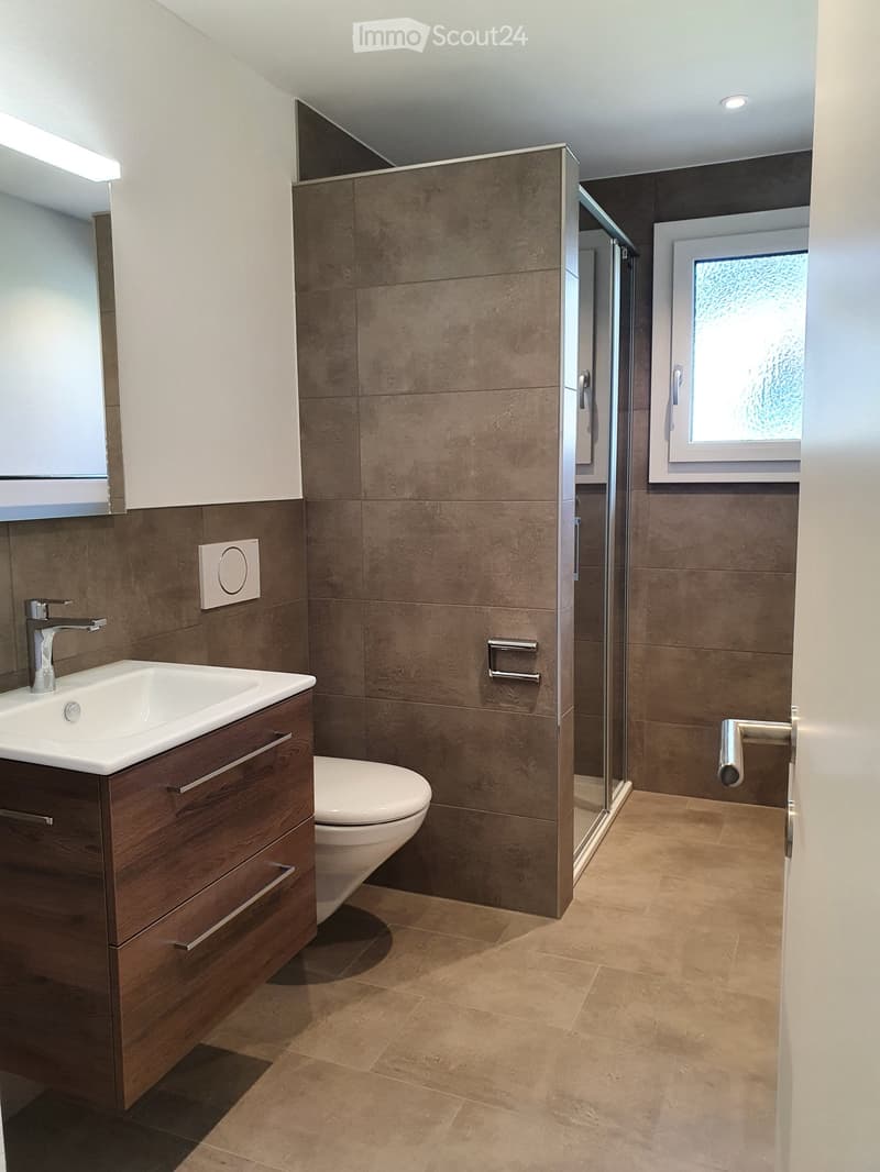 Modern bathroom with beige tiles, white sink, wooden cabinet, and a glass shower enclosure.