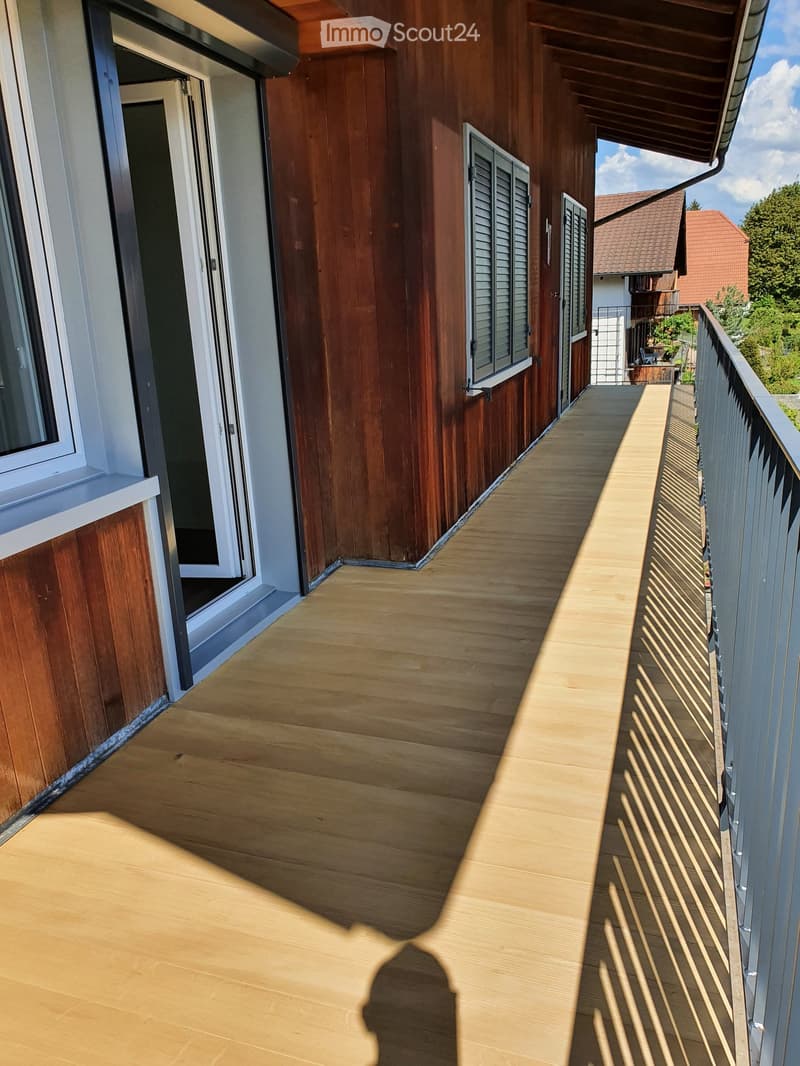 Wooden balcony with a metal railing, wooden floor, and a shadow cast on the floor.