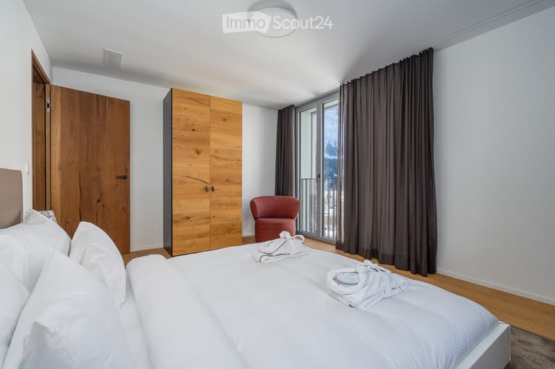 wooden cabinet, white bed, two pillows, a chair, a lamp, windows, curtains