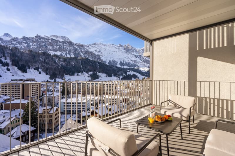 a balcony with a scenic view, modern seating arrangement, outdoor table with fruit platter, clear sky, snowy mountains in the distance