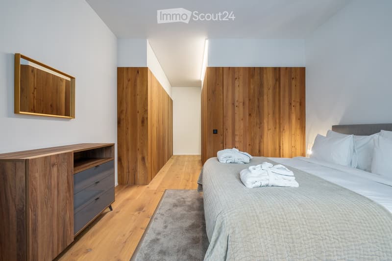 Modern bedroom with wooden panels, grey carpet, wooden dresser, modern bedding, wall-mounted mirror