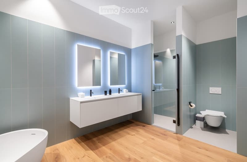 Bathroom with white bathtub, white countertop with double sinks, two large mirrors, glass shower, blue walls