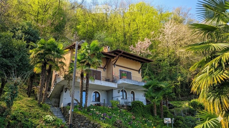 2 story house, brown roof, white walls, balcony, surrounded by trees and plants