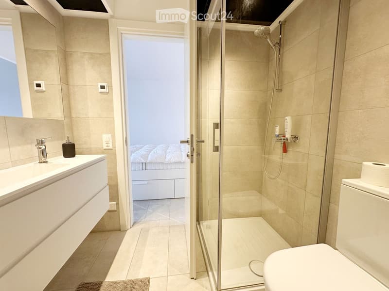 modern bathroom with white tiles, white vanity, glass shower, white toilet, white sink, mirror, soap dispenser, toilet paper