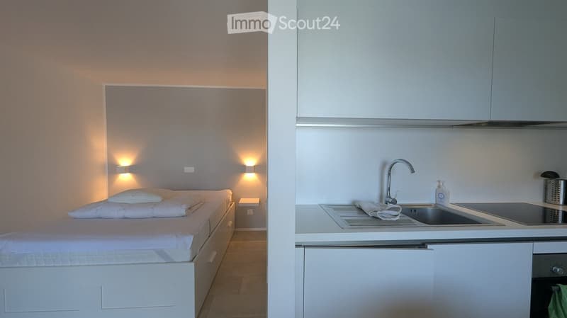 small bedroom with bed, white walls, white bed, white cabinets, sink, dishwasher, stove