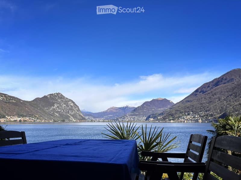 Table with blue tablecloth, two chairs, lake view, mountains in the background
