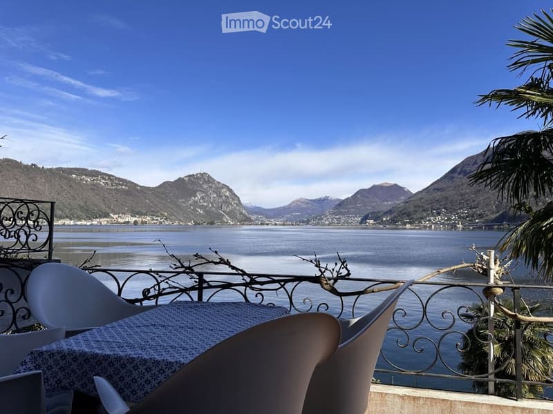 Balcony with table and chairs, metal railing, view of lake and mountains
