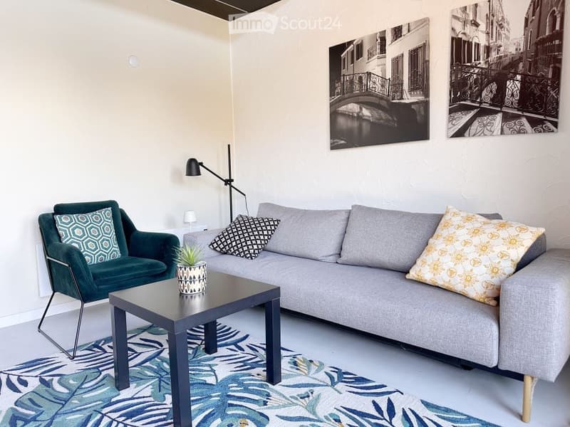 Living room with gray sofa, blue chair, black table, decorative plant, lamp, and two black and white wall art.