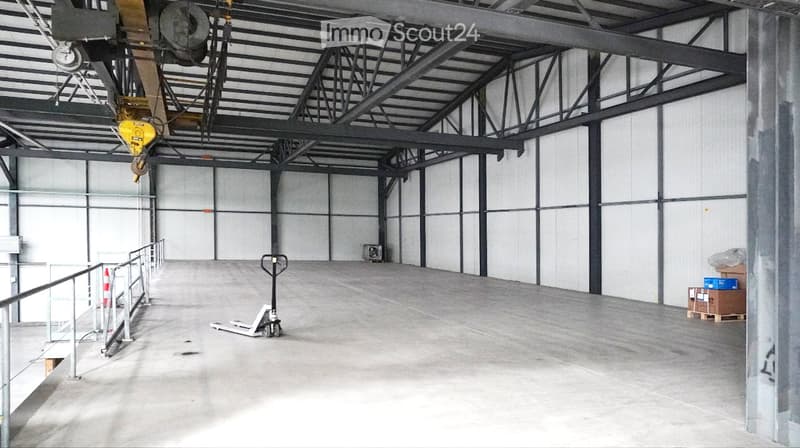 Empty warehouse with concrete floor, metal beams, and a forklift in the center. The walls are white with metal supports, and there are some storage boxes on the right side.