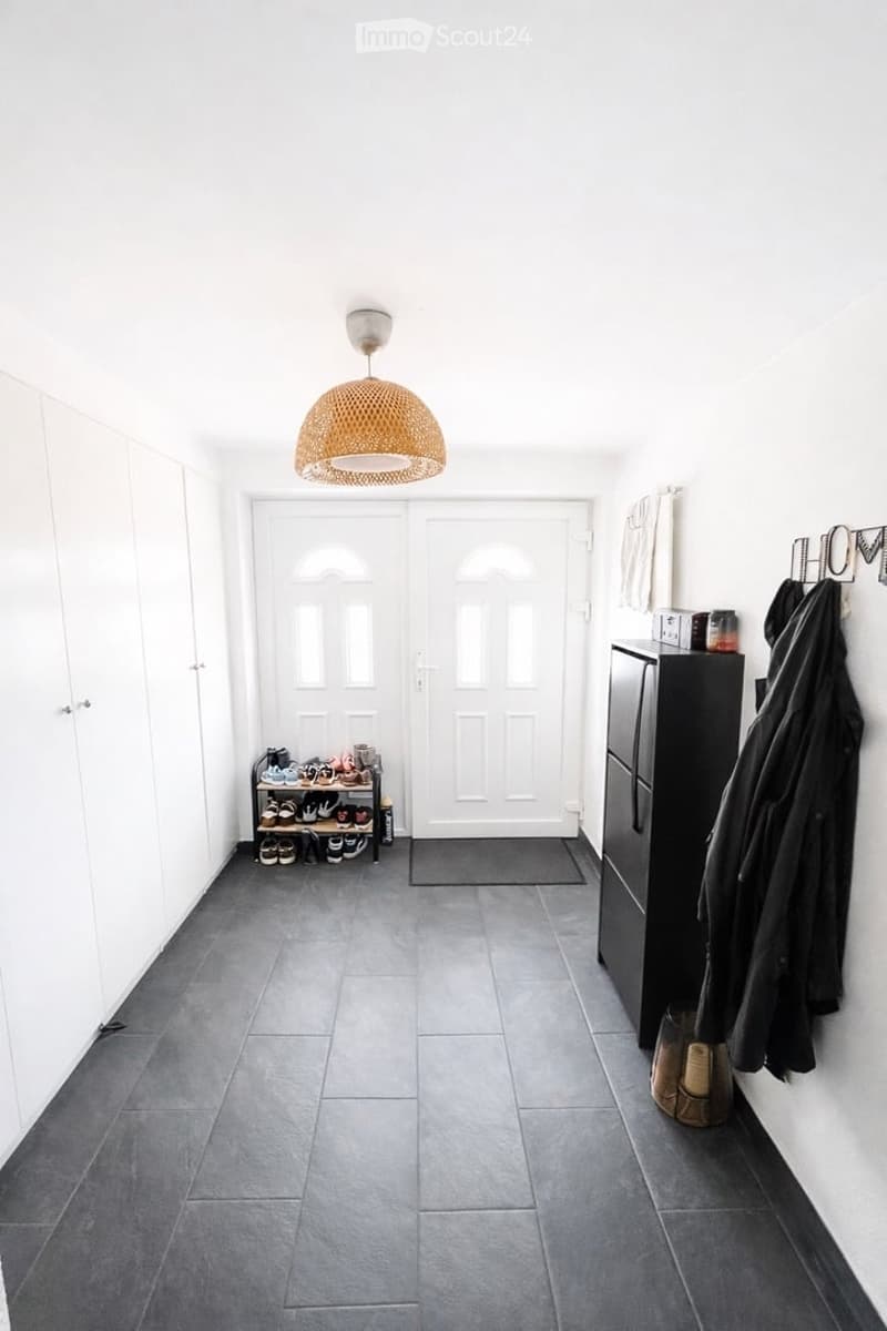 Entrance hall with tiled floor, white walls, double doors, shoe rack, cabinet, hanging coat, lamp