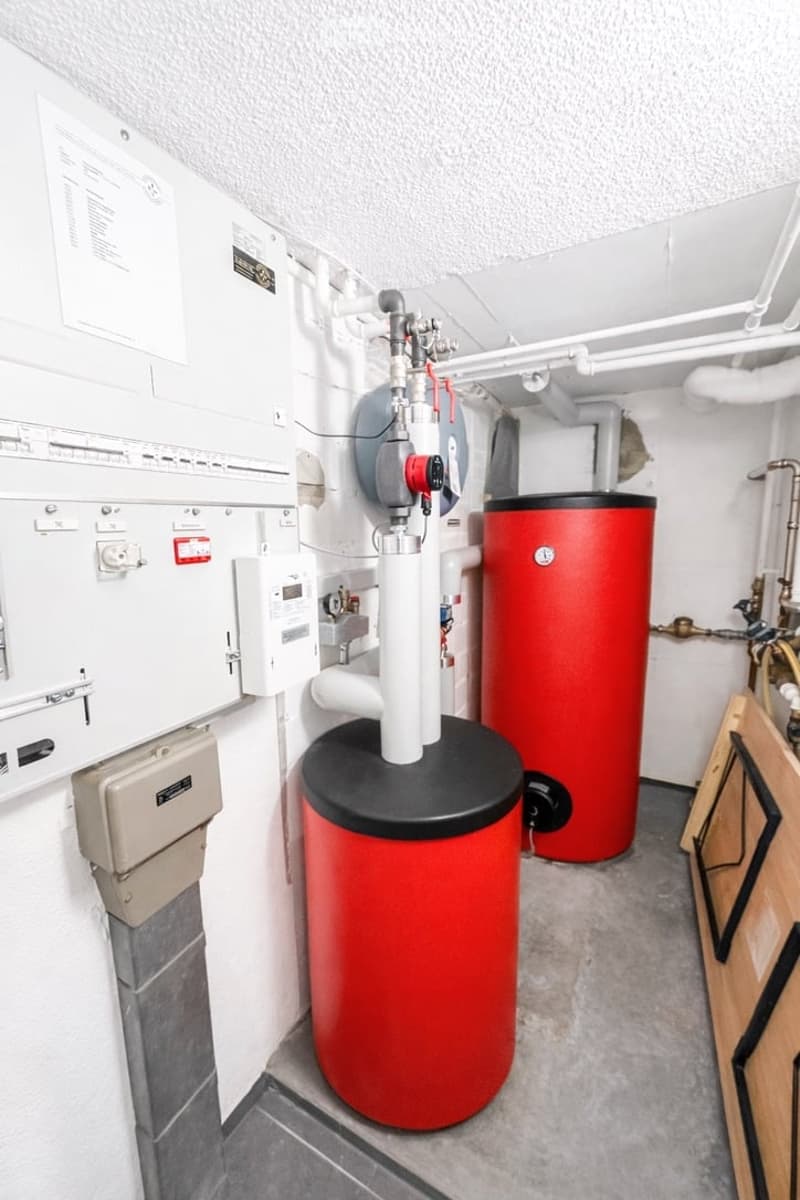 Utility room with two red water heaters, pipes, and electrical panels