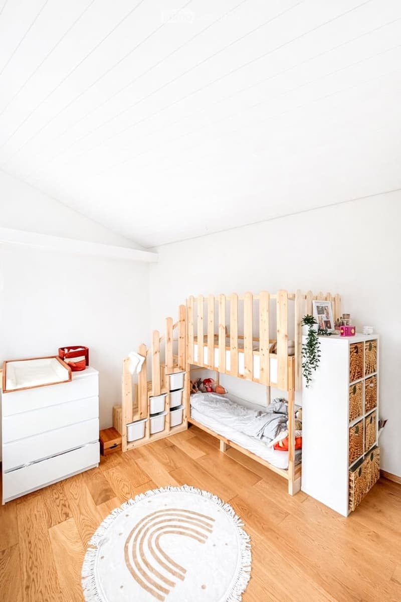 A child's bedroom with a wooden bunk bed, white dresser, and a round rug on the floor.