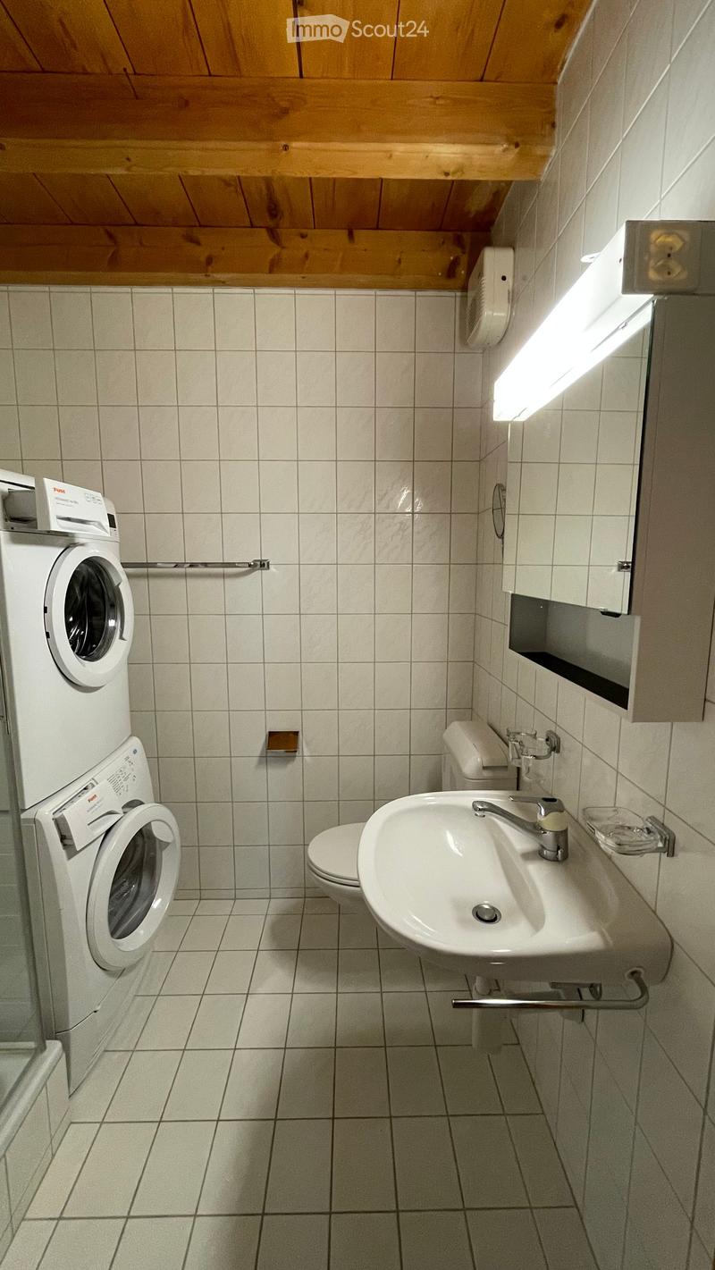 white tiled bathroom with toilet, sink, mirror and washing machine