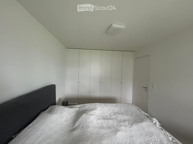 A bedroom with a bed, bedspread, and a wardrobe. The room has white walls and ceiling.